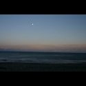 The moon coming up over the ocean at sunset.